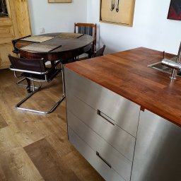 Witold Szostak - Szostak Atelier - Nowoczesna kuchnia: drewniany blat z metalowymi szafkami, okrągły stół z krzesłami, drewniana podłoga i grafiki na ścianach tworzą przytulne wnętrze.