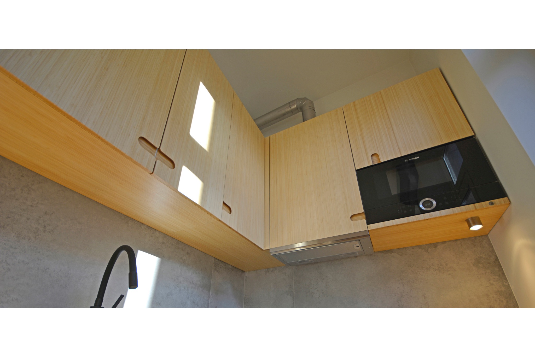 Nowoczesna kuchnia: jasne, drewniane szafki górne z oryginalnymi uchwytami, wbudowany piekarnik Bosch, szary backsplash i czarna bateria. Minimalistyczny design.