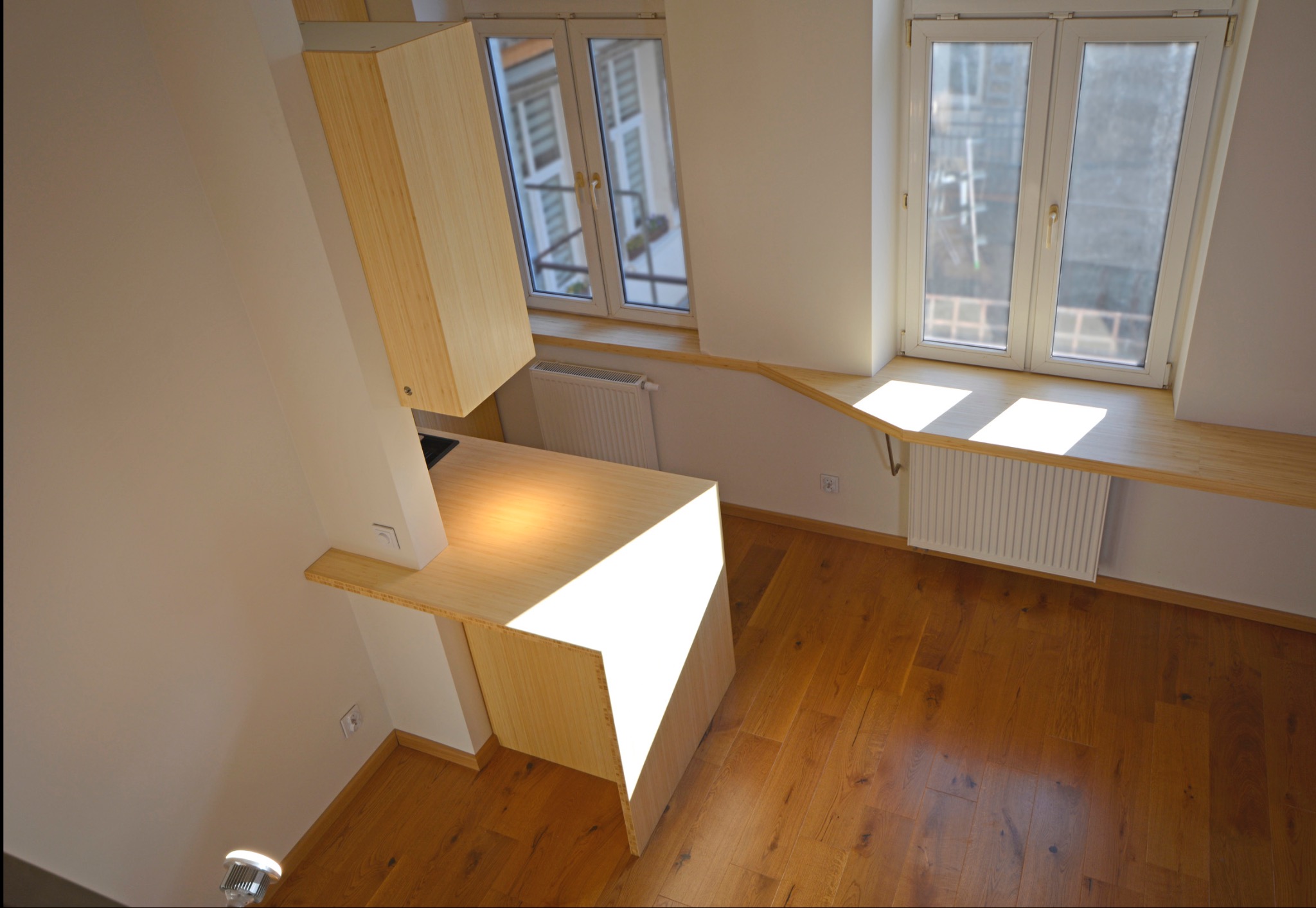 Drewniana zabudowa kuchenna pod skosem z blatem oświetlonym promieniami słońca, widok z góry. Parapety z tego samego drewna.