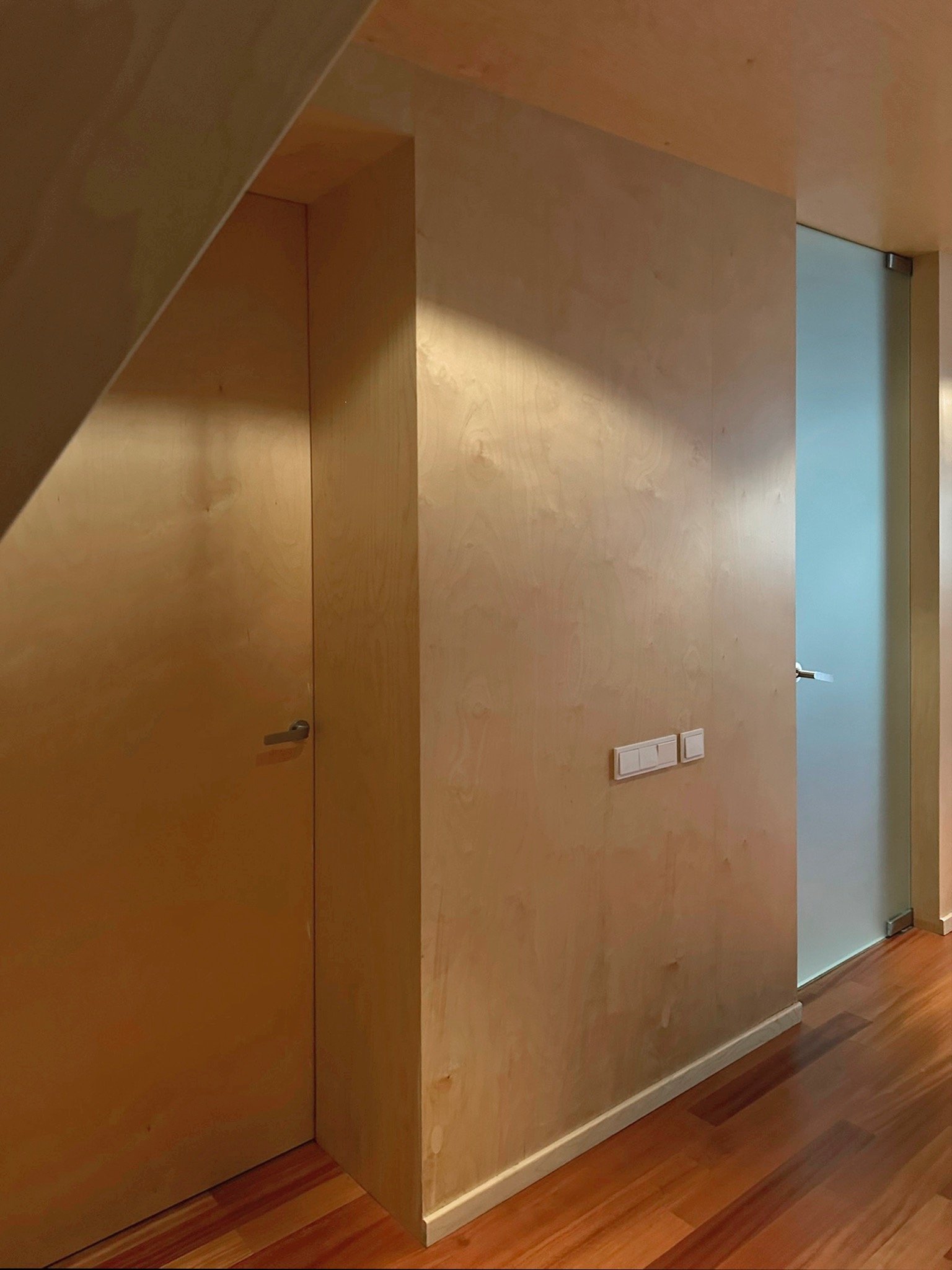 Nowoczesne wnętrze: drewniane ściany z wbudowanymi drzwiami i szklanymi przesuwnymi drzwiami. Parkiet na podłodze, minimalistyczne wykończenie i oświetlenie.