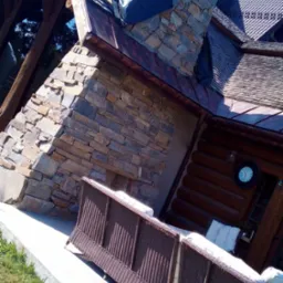 Kamienna elewacja domu z tarasem i widocznym fragmentem dachu zabezpieczonego folią. Na tarasie stoi brązowa sofa.