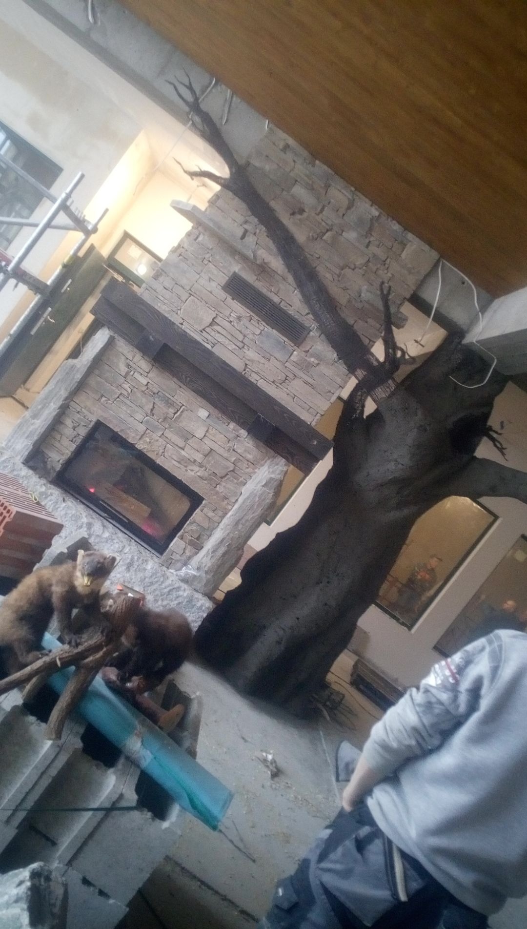 Wnętrze w trakcie wykańczania: murowany kominek z paleniskiem, atrapa drzewa, rusztowanie. Dekoracja z kunami na pierwszym planie.