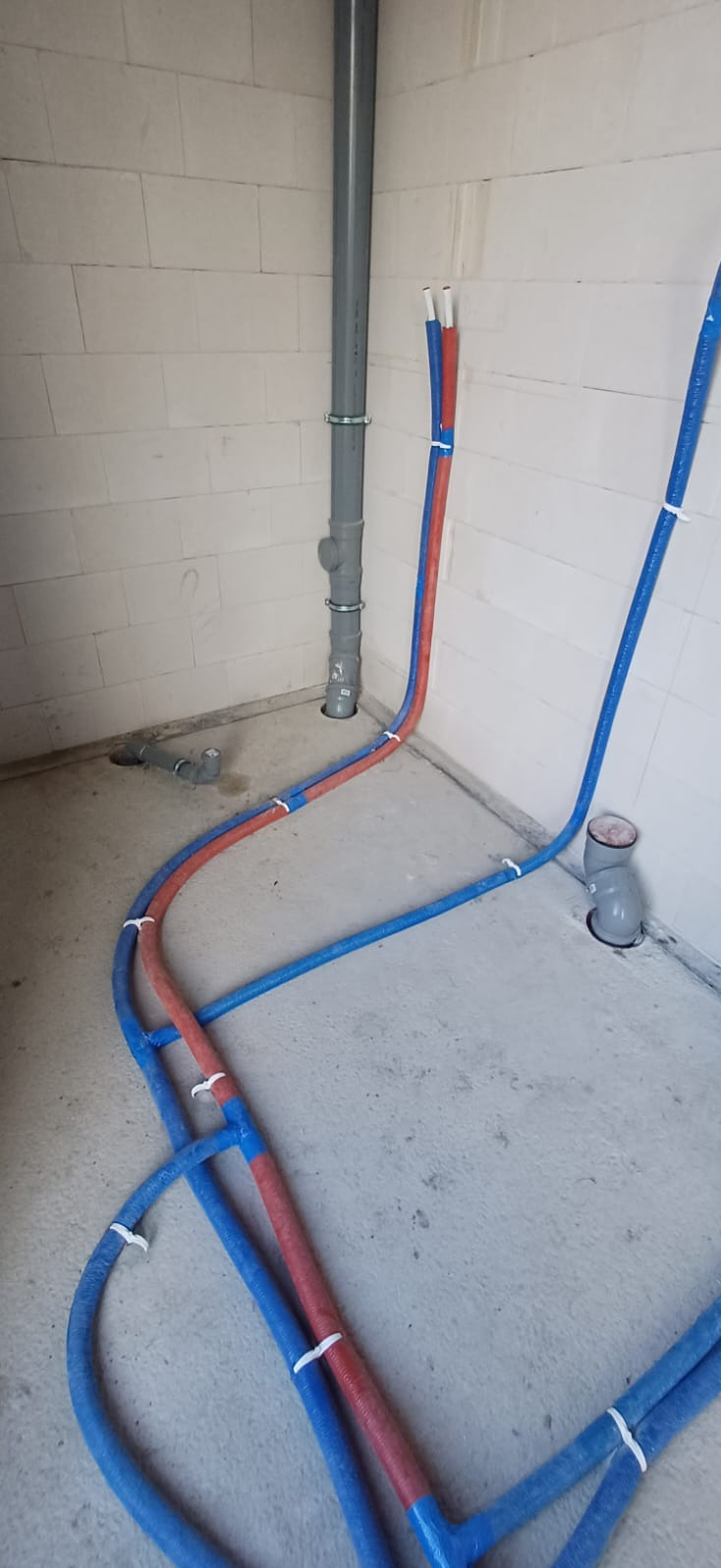 Instalacja rur grzewczych i kanalizacyjnych w surowym wnętrzu we Wrocławiu. Rury w izolacji niebieskiej i czerwonej, pion kanalizacyjny, ściany z betonu komórkowego.