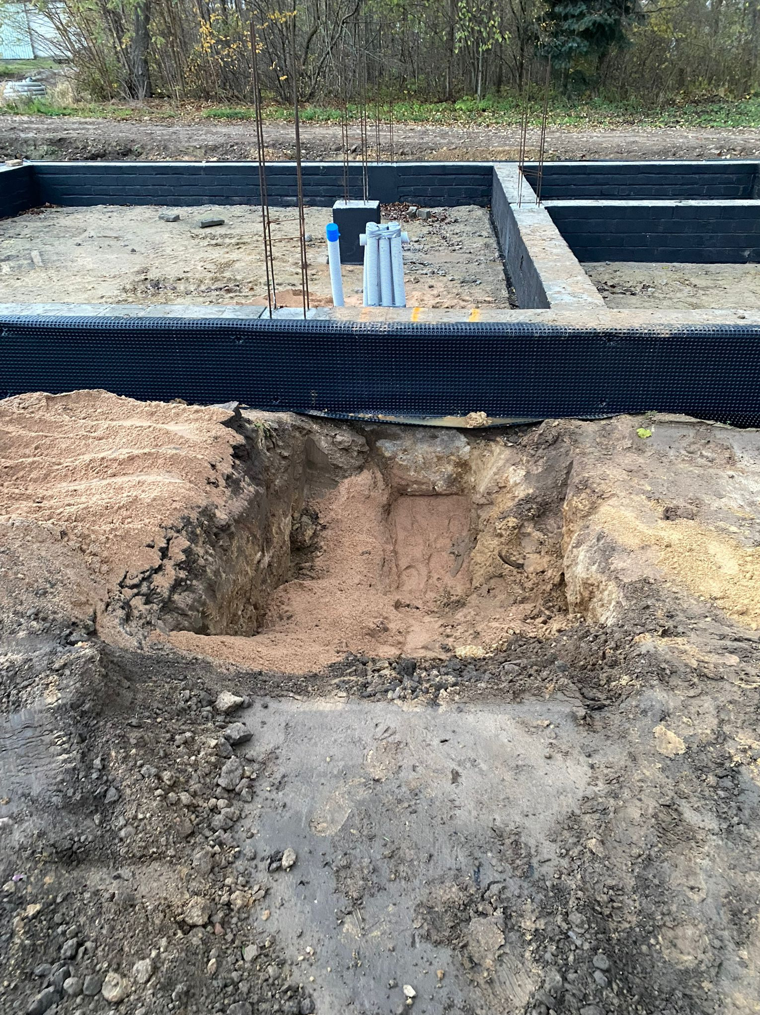 Wykop fundamentów z izolacją, widoczne rury instalacyjne wystające z ziemi. Fundamenty w trakcie budowy, teren budowy, jesienna sceneria.