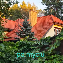 FACHOWIEC PODLASIE - Czerwony dach domu po myciu, widoczny zza zieleni, z ceglanym kominem i dymem. Ujęcie z dołu, podkreślające czystość dachu po zabiegu.