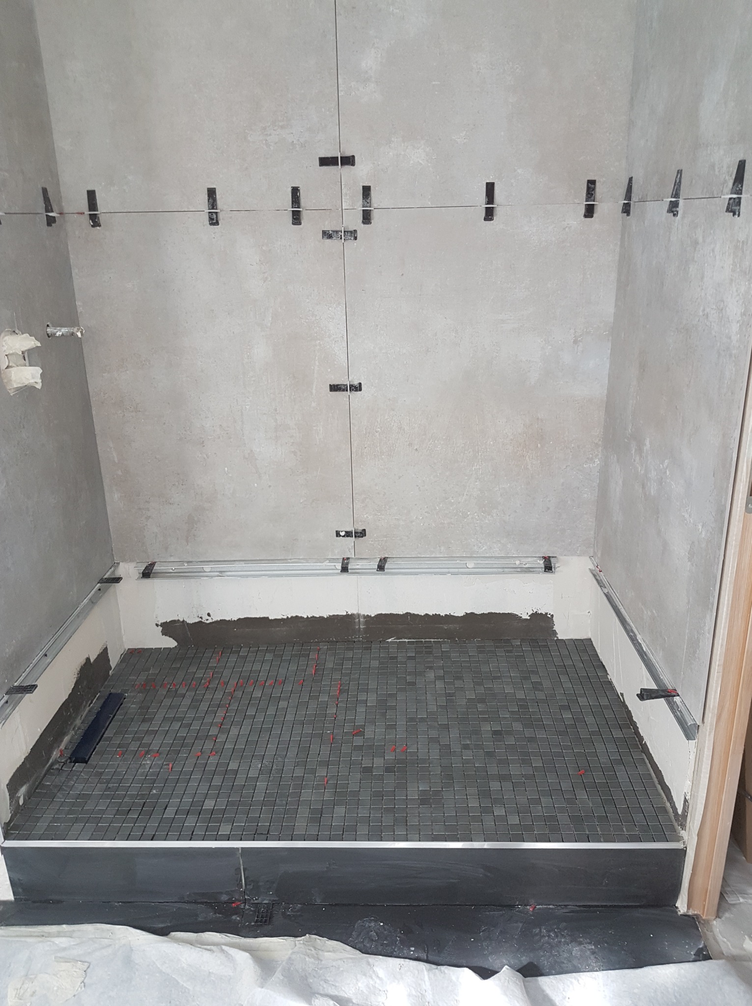 Mozaika ułożona w brodziku kabiny prysznicowej, widoczne listwy wykończeniowe i krzyżyki dystansowe. Ściany surowe, przygotowane do dalszych prac wykończeniowych.