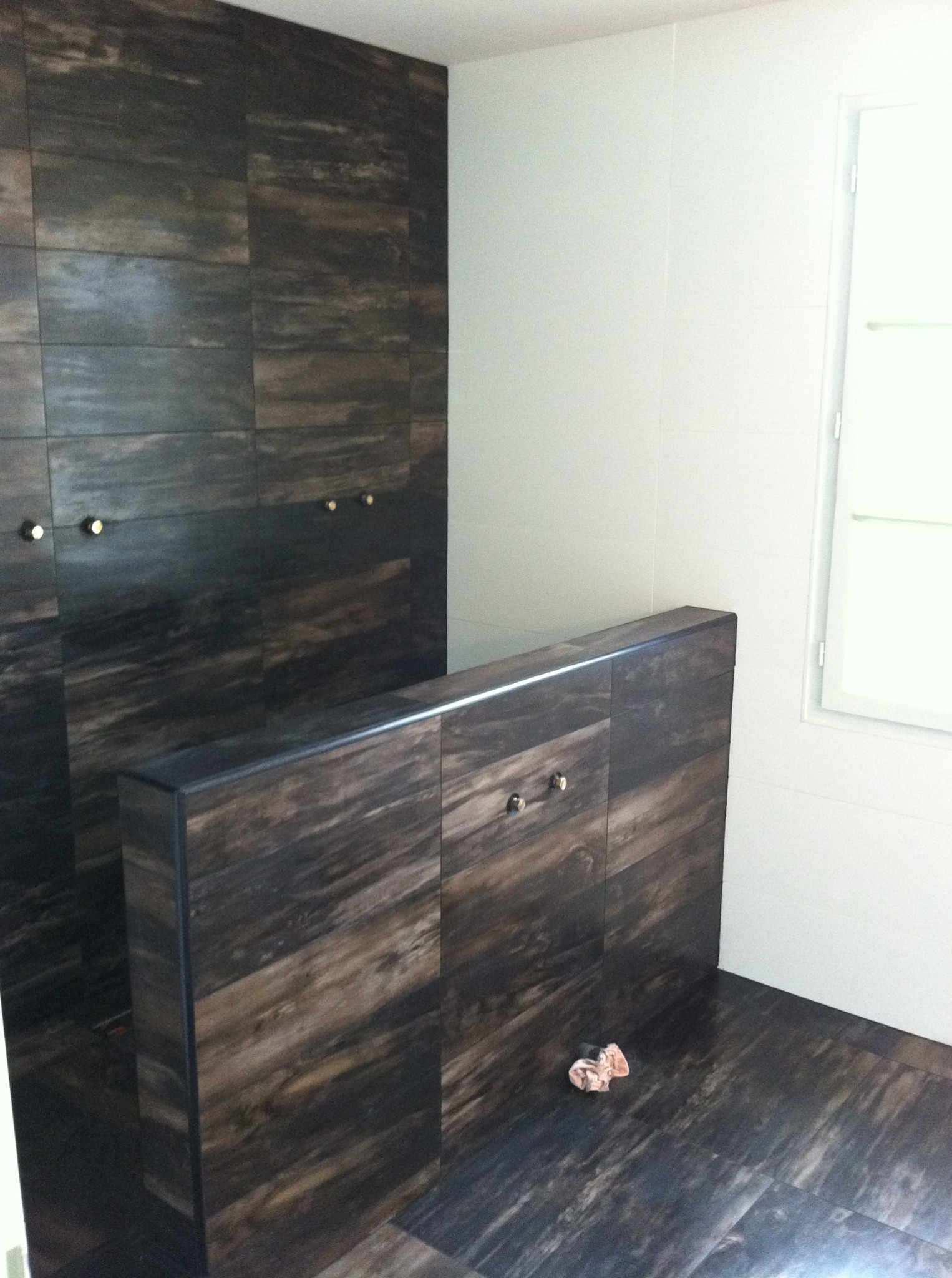 Nowoczesna łazienka z płytkami imitującymi drewno na ścianach i podłodze. Widoczne detale, takie jak złote uchwyty i białe płytki.