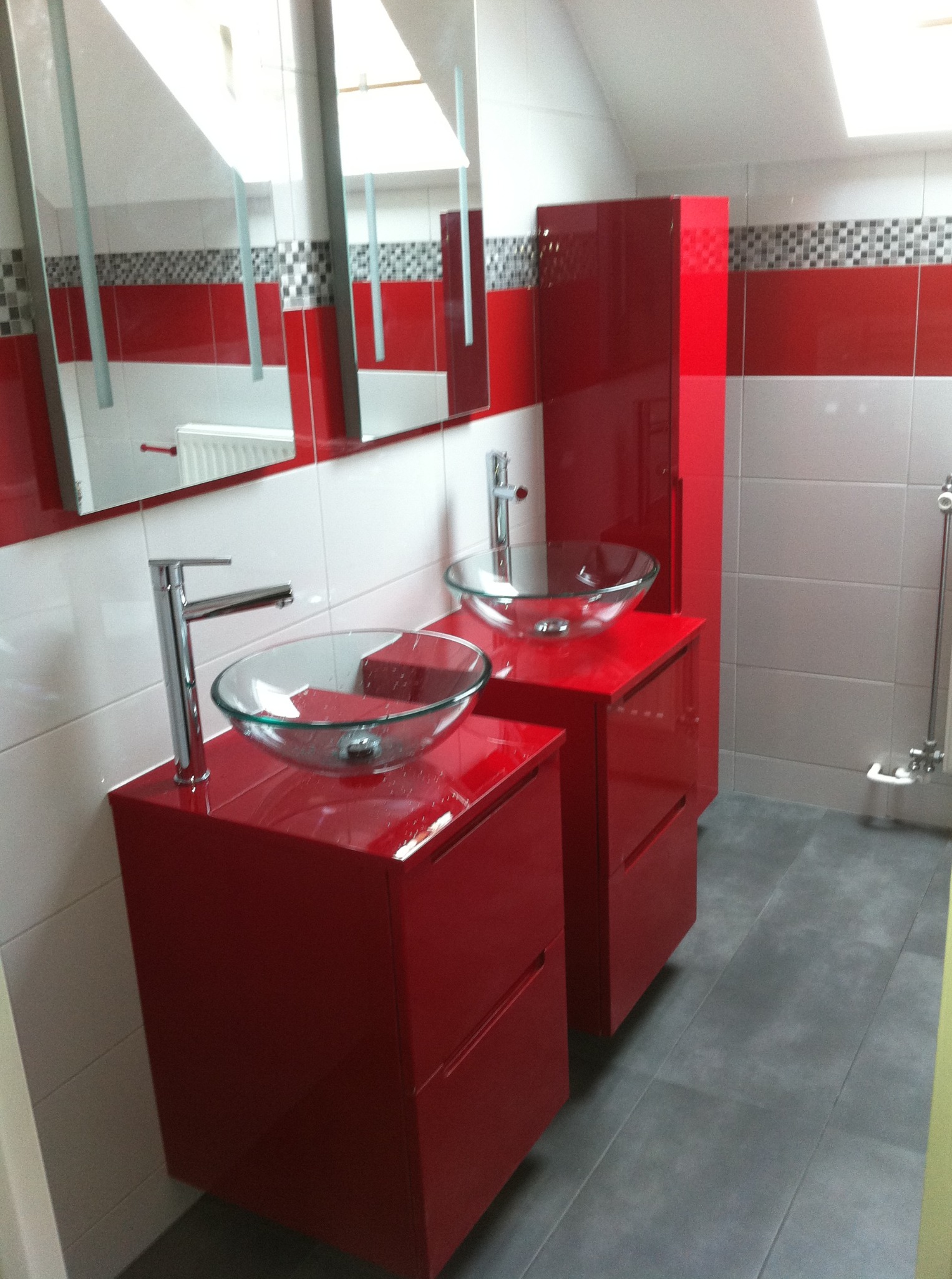 Czerwona, nowoczesna łazienka na poddaszu: dwie szafki z umywalkami ze szkła, lustro i płytki w odcieniach bieli, czerwieni i szarości. Wykończenie z dbałością o detale.