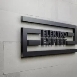 Eleganckie, trójwymiarowe logo 'Elektro Expert' w kolorze grafitowym, umieszczone na jasnoszarej, teksturowanej ścianie z kamiennych płytek. Ujęcie z perspektywy.