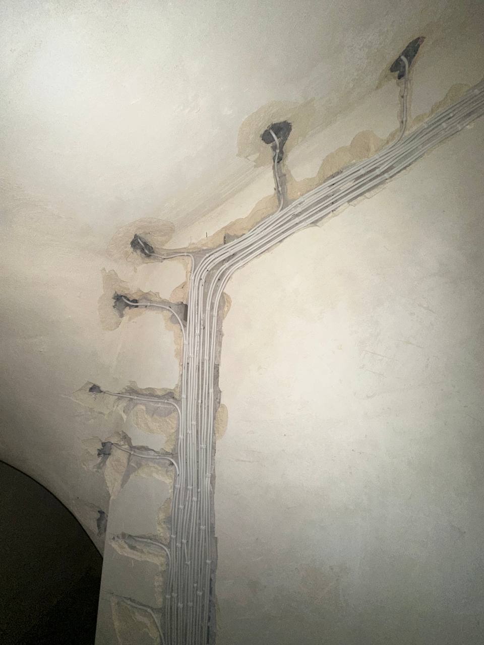 Białe kable elektryczne ułożone w bruzdach na ścianie i suficie budynku w trakcie remontu, z widocznymi puszkami instalacyjnymi.