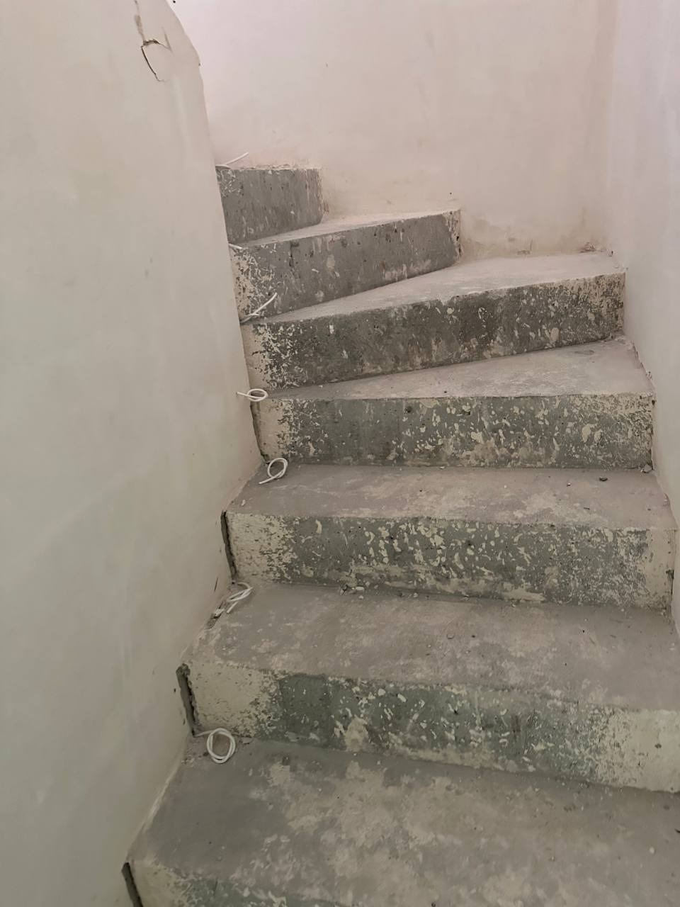 Surowe, betonowe schody spiralne w trakcie prac wykończeniowych z wystającymi przewodami elektrycznymi do oświetlenia.