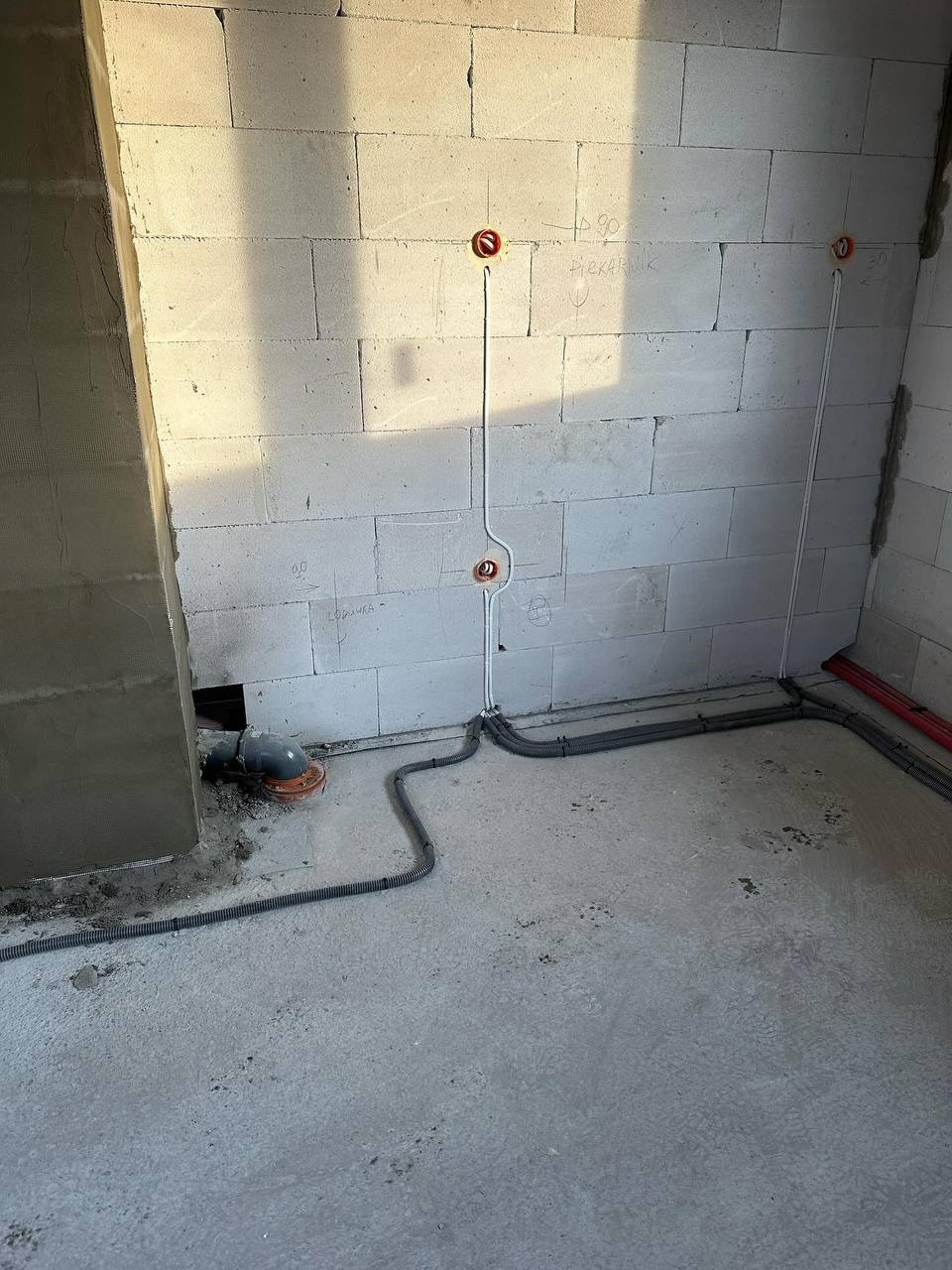 Surowy stan: instalacja elektryczna w peszlach i wypusty pod gniazdka na ścianie z betonu komórkowego. Widoczne oznaczenia wysokości gniazdek.
