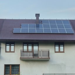Piotr Górka - Dom z brązowym dachem krytym blachodachówką i panelami słonecznymi. Na elewacji balkon z drewnianą balustradą i okna z brązowymi ramami.