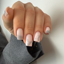 IBBEAUTY Sp.z o.o. - Dłoń z jasnoróżowym manicure hybrydowym, zdobionym srebrnym wzorem siateczki. Kwadratowy kształt paznokci i delikatne zdobienie dodają elegancji.