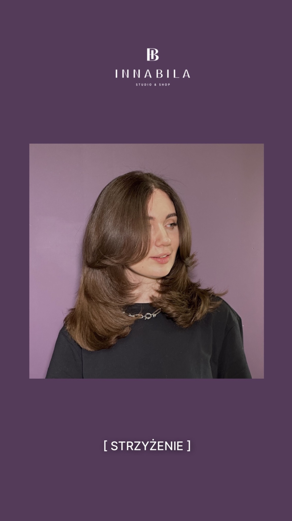 Portret kobiety z brązowymi włosami po strzyżeniu w salonie, z delikatnym uśmiechem i srebrnym naszyjnikiem na tle fioletowej ściany.