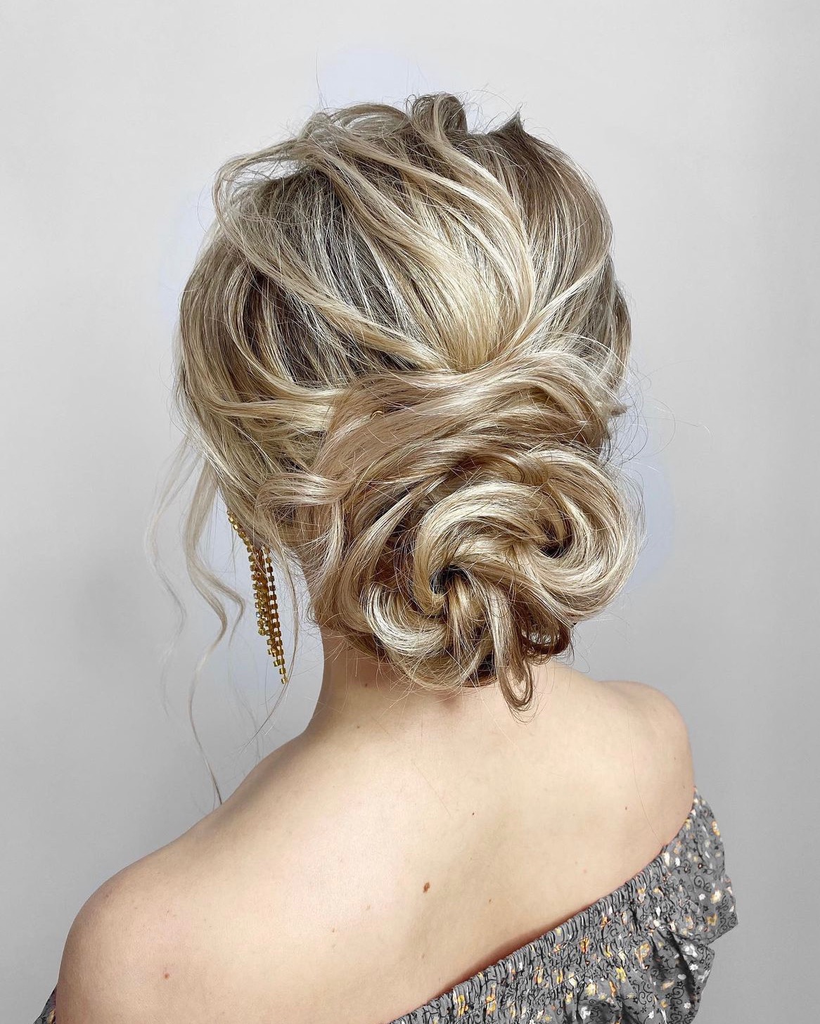 Upięcie blond włosów z warkoczem i luźnymi pasmami, widok z tyłu, odsłonięte ramię z delikatną biżuterią. Fryzura na specjalną okazję.