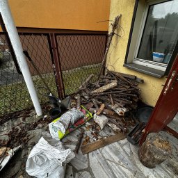 CleanStrike - Sterta gałęzi, worki ziemi i narzędzia ogrodnicze przy żółtej ścianie budynku. Widoczne liście i resztki roślinne na kamiennej posadzce.