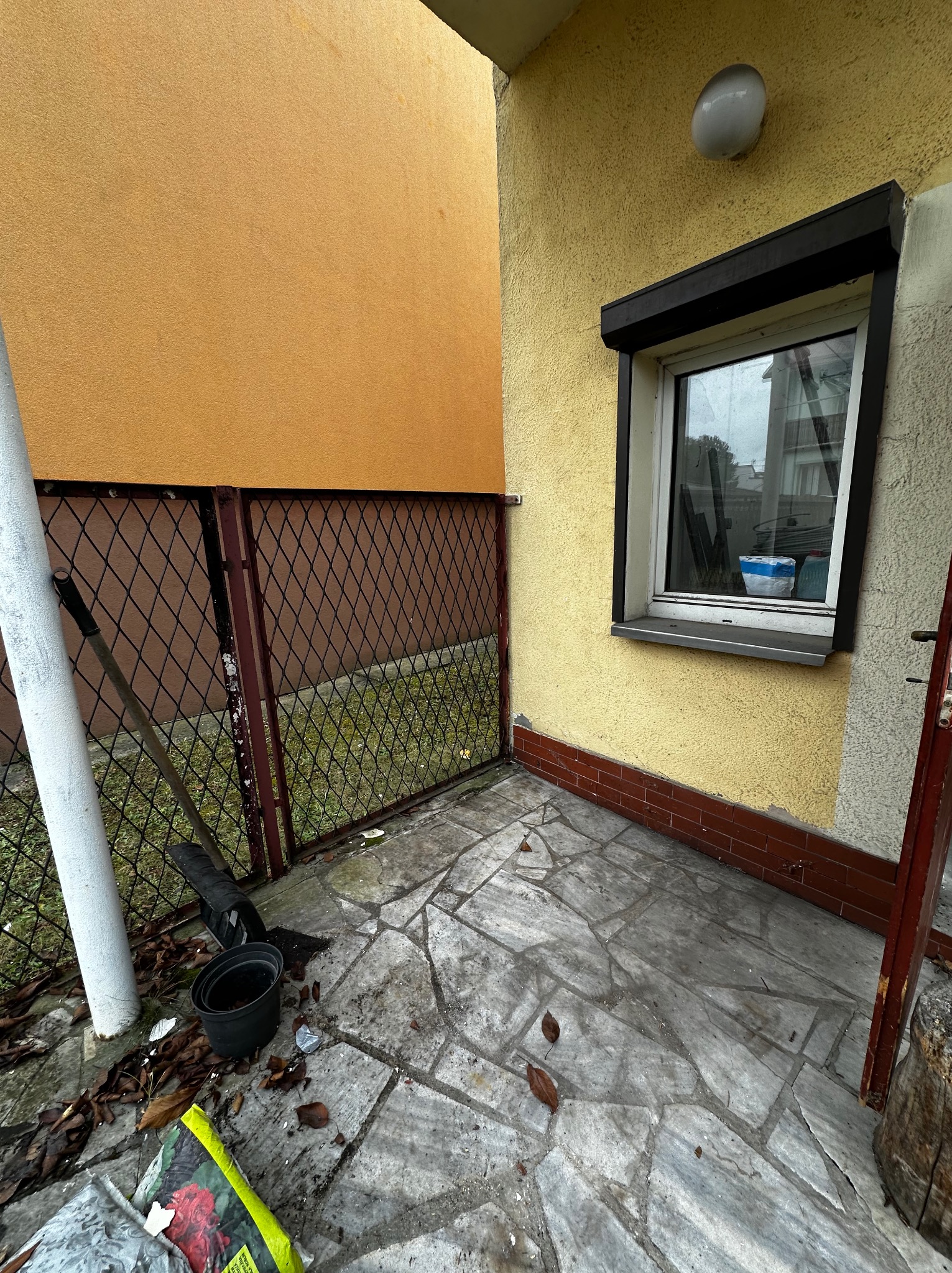 Zakamarek z kostką brukową, narzędzia ogrodnicze, doniczka i worek ziemi. Przygotowania do prac ogrodowych na małej przestrzeni.