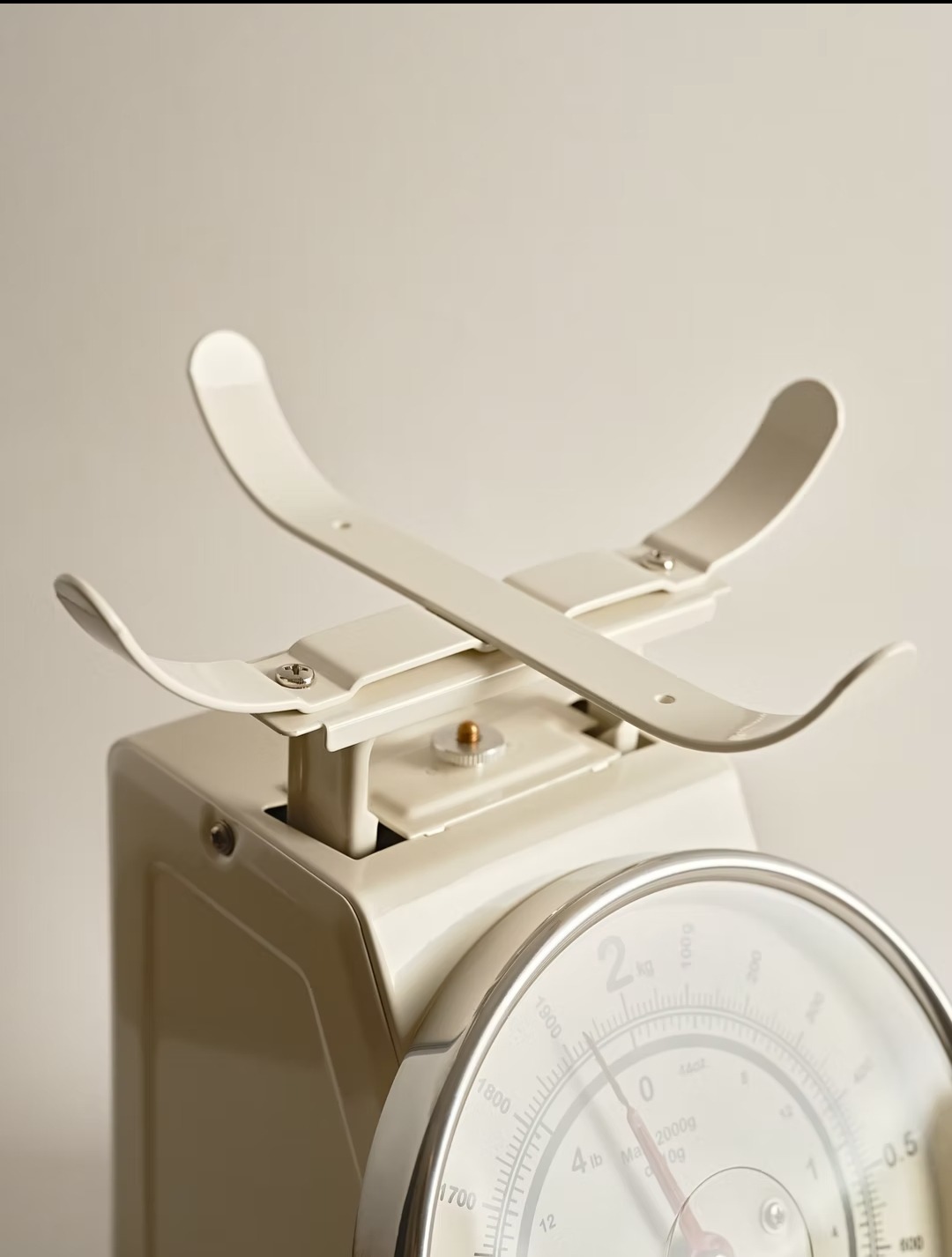 Beżowa waga kuchenna z metalowym ramieniem i tarczą z podziałką. Ujęcie z bliska, ukazujące detale konstrukcji i precyzję wykonania.