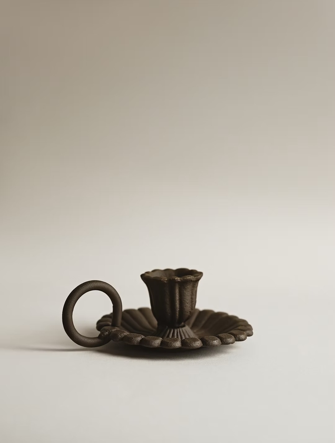 Elegancki, brązowy świecznik z uchwytem w kształcie pierścienia, na białym tle. Minimalistyczna fotografia produktowa z delikatnym cieniem.