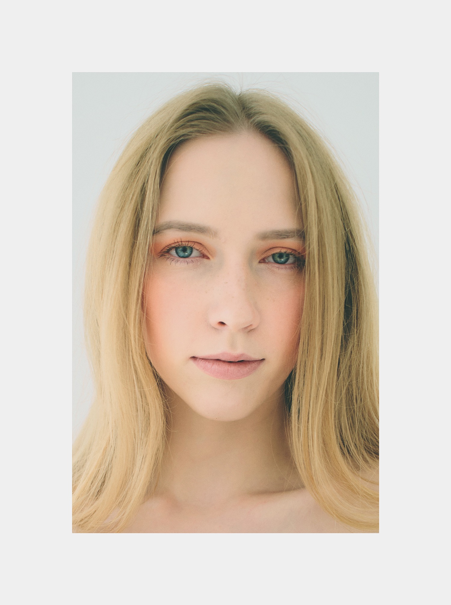 Portret młodej kobiety o jasnych włosach i delikatnym makijażu oczu w odcieniach brzoskwini, na jasnym tle. Ujęcie centralne, skupione na twarzy.