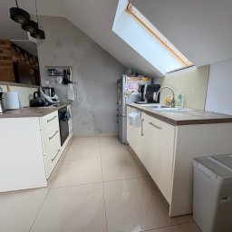 BEE PERFECT - Jasna kuchnia na poddaszu z oknem dachowym. Zabudowa meblowa w odcieniach beżu z drewnianym blatem. Na blacie zlewozmywak i akcesoria kuchenne. Widoczny fragment lodówki i pojemnik.