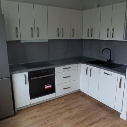 BEE PERFECT - Jasna kuchnia z szarym blatem i sprzętem AGD, widok na zabudowę kuchenną od strony okna z drewnianym parapetem, minimalistyczny design.