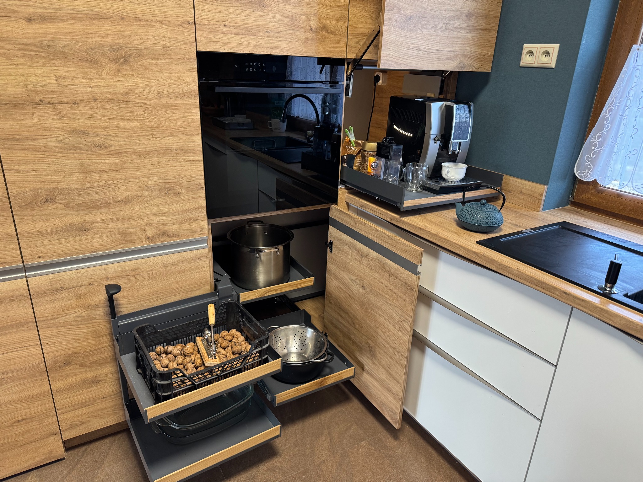 Nowoczesna kuchnia z drewnianymi frontami, wysuwanymi półkami i szufladami, na których znajdują się akcesoria kuchenne i produkty spożywcze.