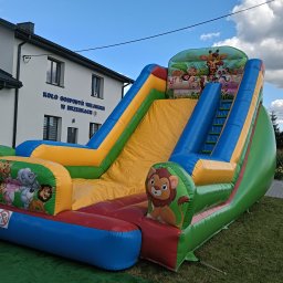 KROKODYLEK - Kolorowa, dmuchana zjeżdżalnia z motywem zwierząt na tle budynku z napisem 'Koło Gospodyń Wiejskich'.