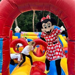 KROKODYLEK - Dzieci bawią się w dmuchanym zamku z animatorem przebranym za postać z bajki. Kolorowy zamek z tunelem i zjeżdżalnią, w tle drzewa.