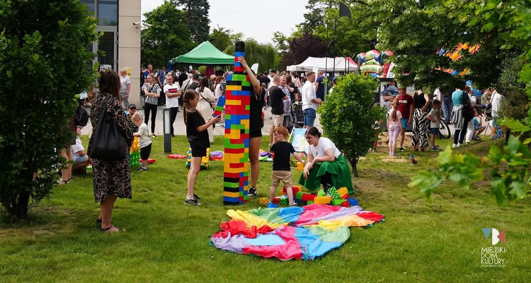 Animacje dla dzieci na świeżym powietrzu: grupa dzieci buduje wieżę z kolorowych klocków, obok leży tęczowa chusta animacyjna, w tle widoczni inni uczestnicy.