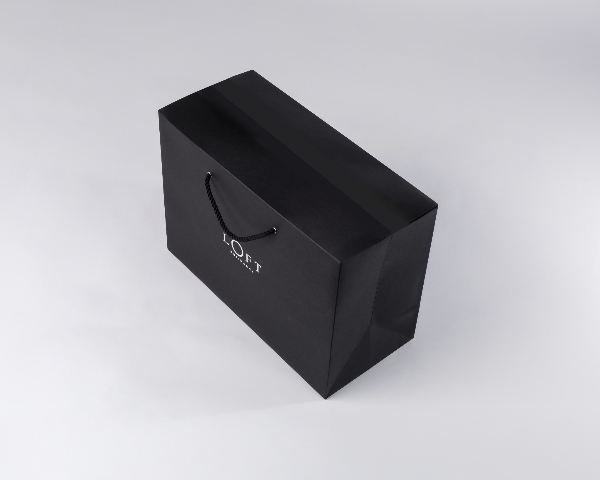 Minimalistyczne ujęcie z góry: czarna torba prezentowa LOFT z matową powierzchnią i sznurkowymi uchwytami na białym tle. Elegancka kompozycja w stylu premium.