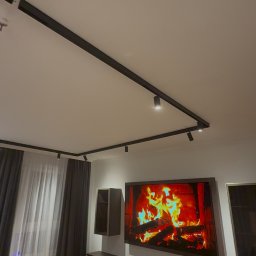 MK_TRO - Nowoczesne oświetlenie szynowe z reflektorami punktowymi w salonie z telewizorem i meblami w odcieniach brązu. Minimalistyczny design, ciepłe światło.