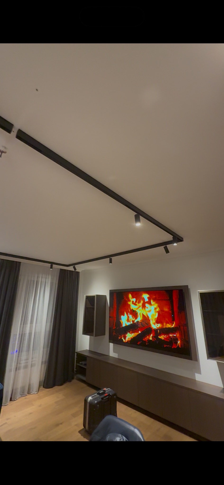 Nowoczesne oświetlenie szynowe z reflektorami punktowymi w salonie z telewizorem i meblami w odcieniach brązu. Minimalistyczny design, ciepłe światło.