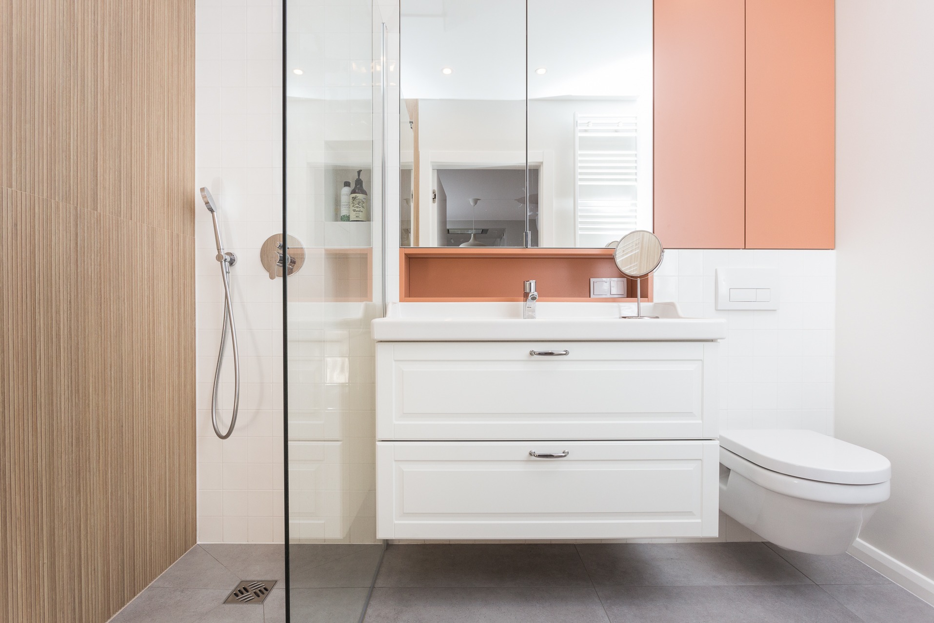 Biała szafka łazienkowa z umywalką i lustrem w odcieniach bieli i brzoskwini, minimalistyczny design, szklana kabina prysznicowa z chromowaną armaturą.