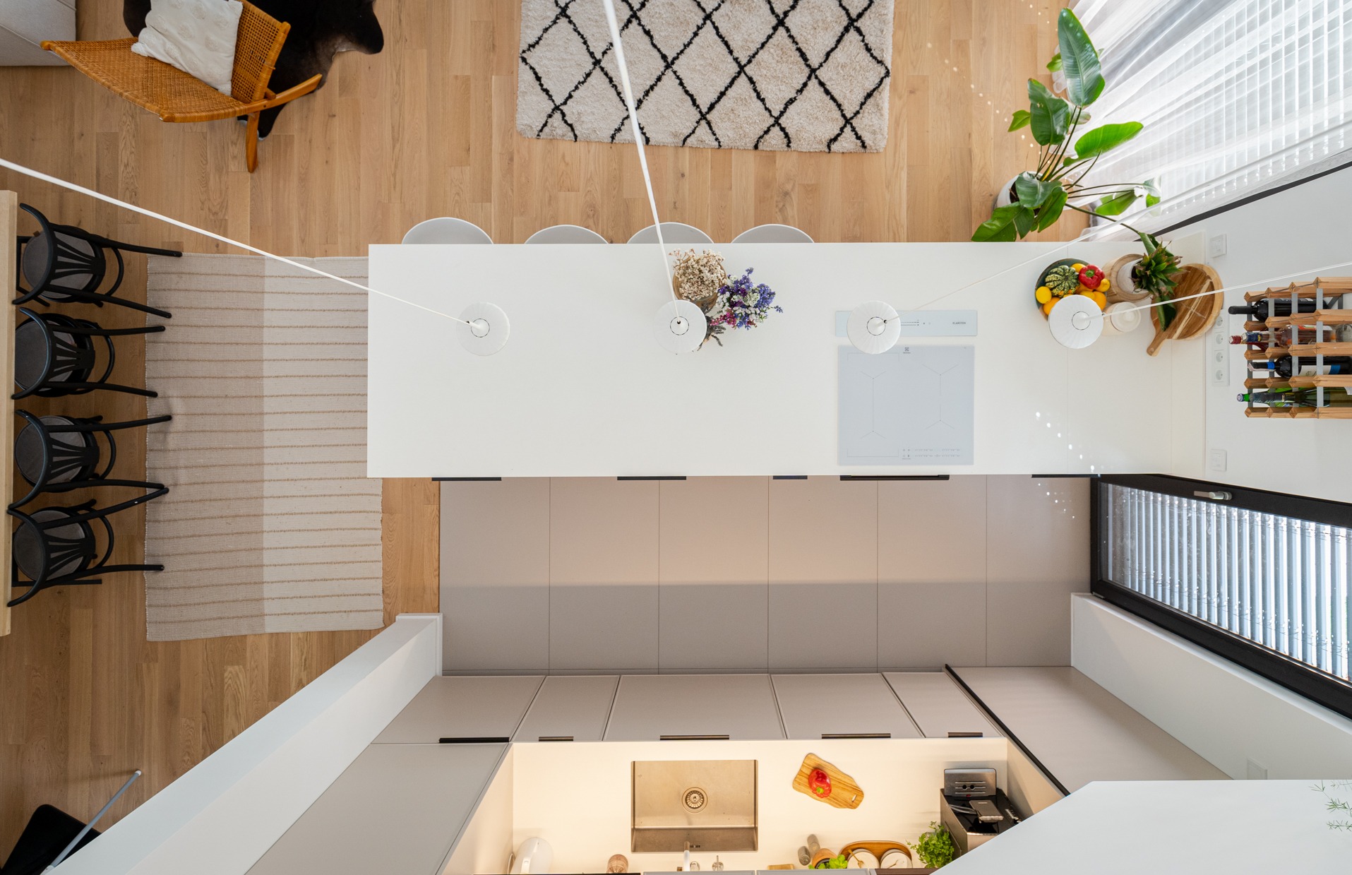 Nowoczesna kuchnia z wyspą, widok z góry. Jasne drewno, białe blaty, szare szafki. Minimalistyczne lampy, rośliny doniczkowe i dekoracje.