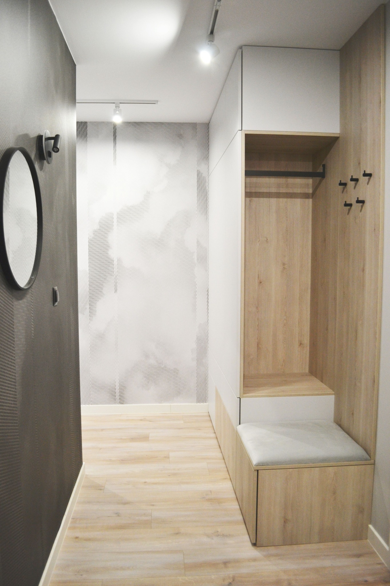 Nowoczesna zabudowa przedpokoju na wymiar w Kraków. Szafa z siedziskiem i wieszakami, biało-drewniane wykończenie, minimalistyczny design, subtelne oświetlenie.