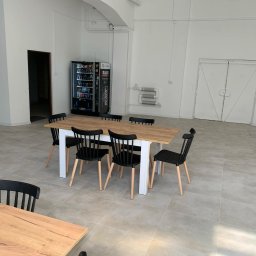 Firma Budowlana TOM-BUD TOMASZ PRZYCHODZEŃ - Jasna, przestronna sala z płytkami podłogowymi, stołem z krzesłami i automatem z napojami. Minimalistyczny wystrój, neutralna kolorystyka.
