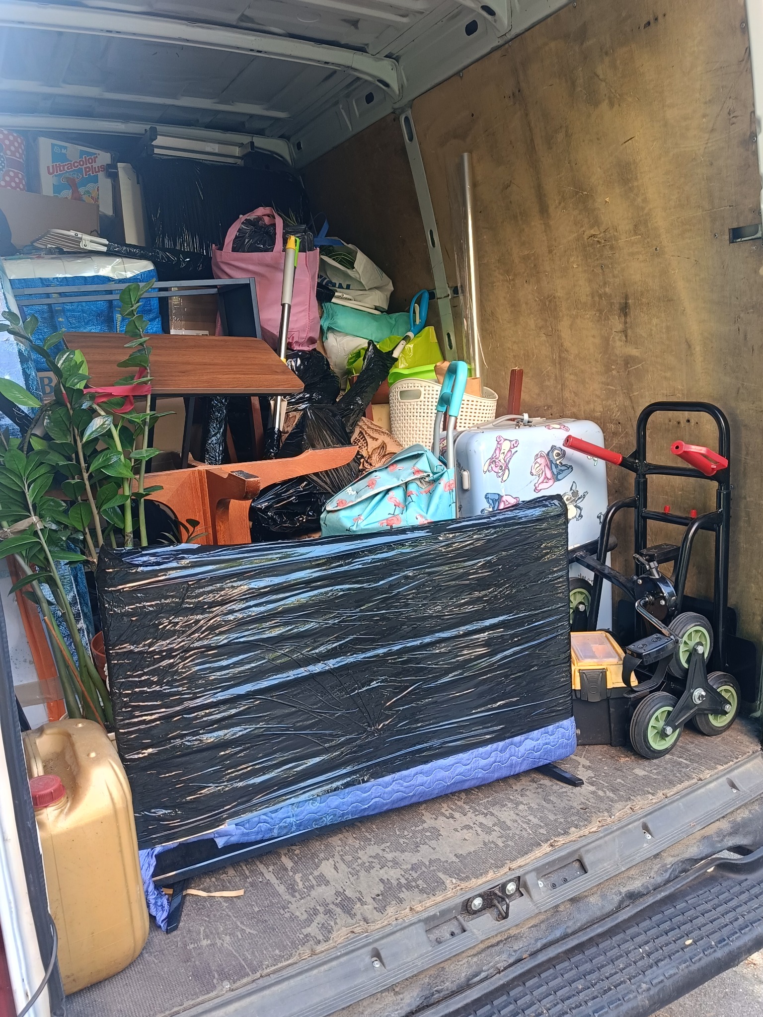 Wnętrze busa załadowane meblami, rośliną doniczkową, sprzętem AGD i osobistymi rzeczami przygotowanymi do transportu. Widoczny wózek transportowy.