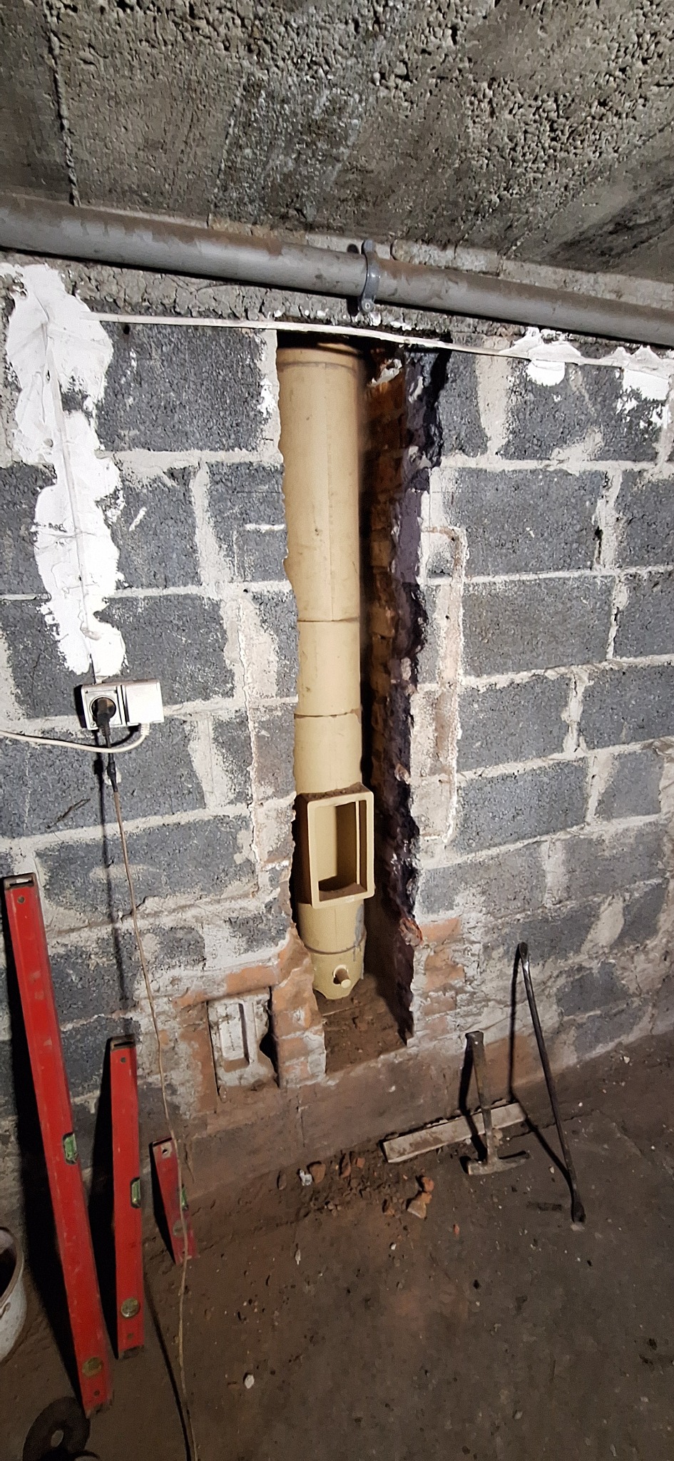 Montaż pionowego przewodu kominowego z otworem rewizyjnym w bloku z szarej cegły. Widoczne narzędzia i poziomice w pomieszczeniu.