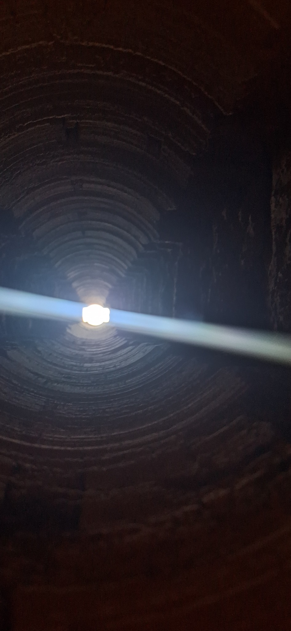 Wnętrze ceglanego komina z widocznym snopem światła wpadającym z góry. Perspektywa z dołu, ukazująca koncentryczne kręgi cegieł.