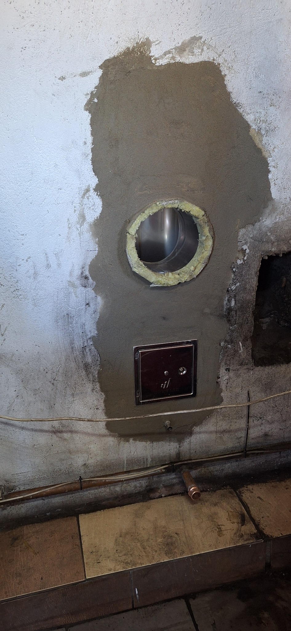 Montaż wkładu kominowego z zabezpieczeniem ogniochronnym i rewizją. Świeżo otynkowane, surowe wykończenie. Widoczne przewody i fragment podłogi.