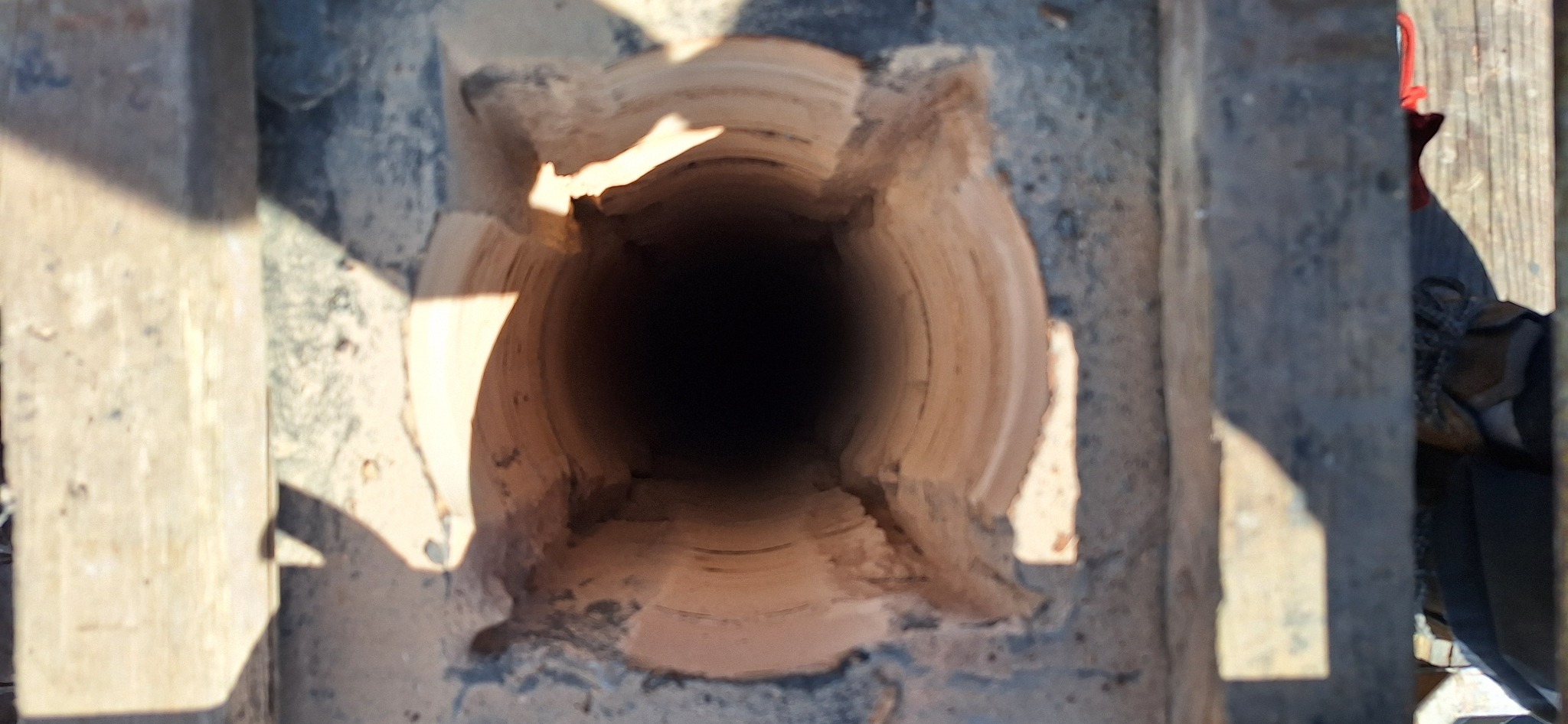 Wnętrze komina z widocznymi ceramicznymi wkładami, uchwycone z góry. Elementy konstrukcyjne i fragmenty butów widoczne w tle. Komin w trakcie budowy/remontu.