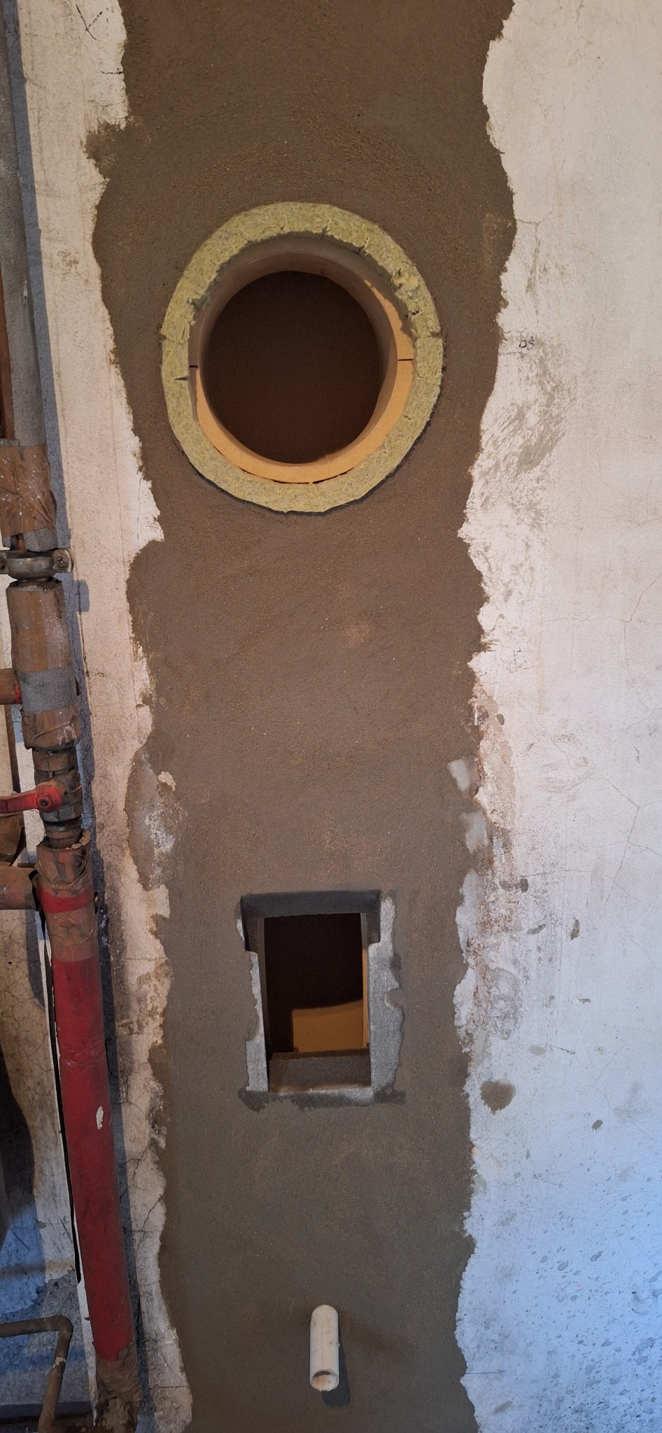 Otwory kominowe po remoncie w Czarkowie, jeden okrągły z izolacją, drugi kwadratowy, oba obrobione zaprawą. Widoczne rury i fragment ściany.