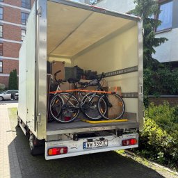 BOXERSI GROUP SPÓŁKA Z OGRANICZONĄ ODPOWIEDZIALNOŚCIĄ - Otwarta paka busa transportowego z dwoma rowerami i kartonami w środku. Rejestracja WW 559UC. Tło: budynek mieszkalny i zieleń. Słoneczny dzień.