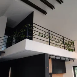 Nowoczesne schody metalowe z balustradą, zdobione pnącą roślinnością, w minimalistycznym wnętrzu z czarno-białą kolorystyką i drewnianymi akcentami.