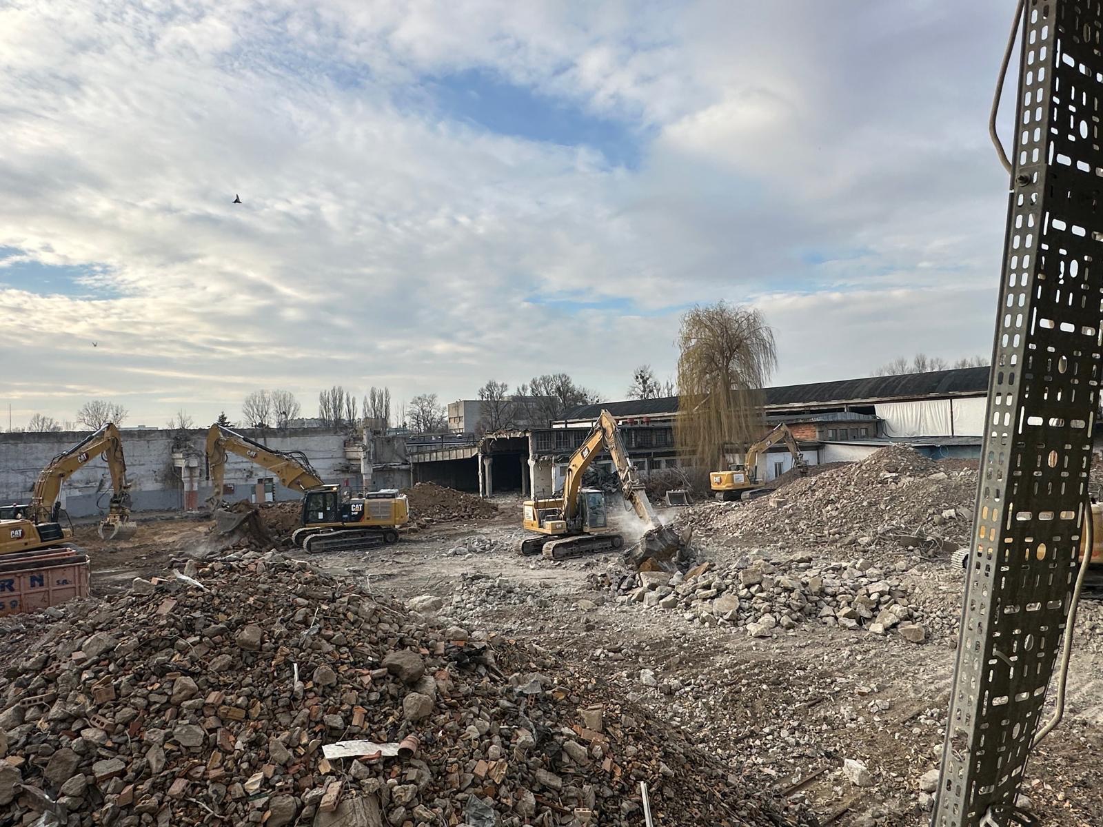 Rozbiórka budynku w Zaborowie. Kilka koparek CAT pracuje na gruzowisku, w tle fragmenty zburzonej konstrukcji i drzewo. Pochmurne niebo.