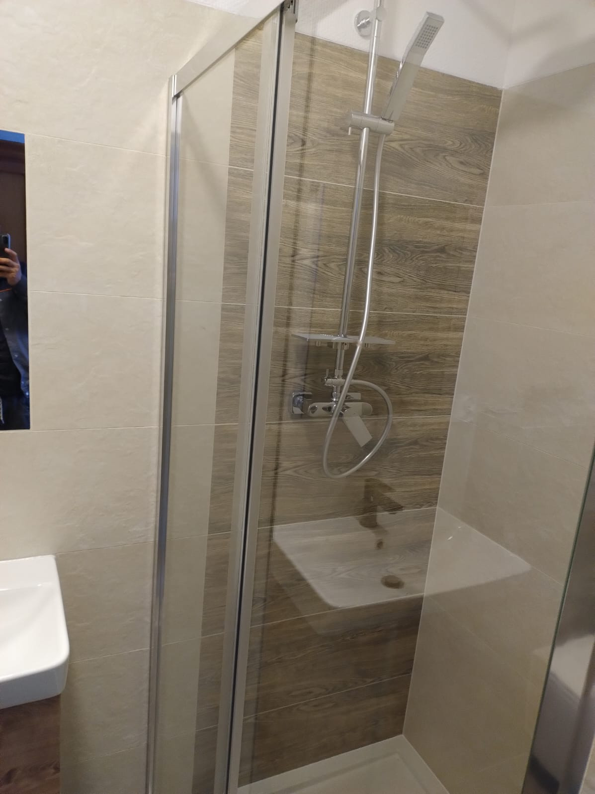 Wykończona łazienka: kabina prysznicowa z deszczownicą, umywalka nablatowa i płytki imitujące drewno na ścianie. Nowoczesny design z dbałością o detale.