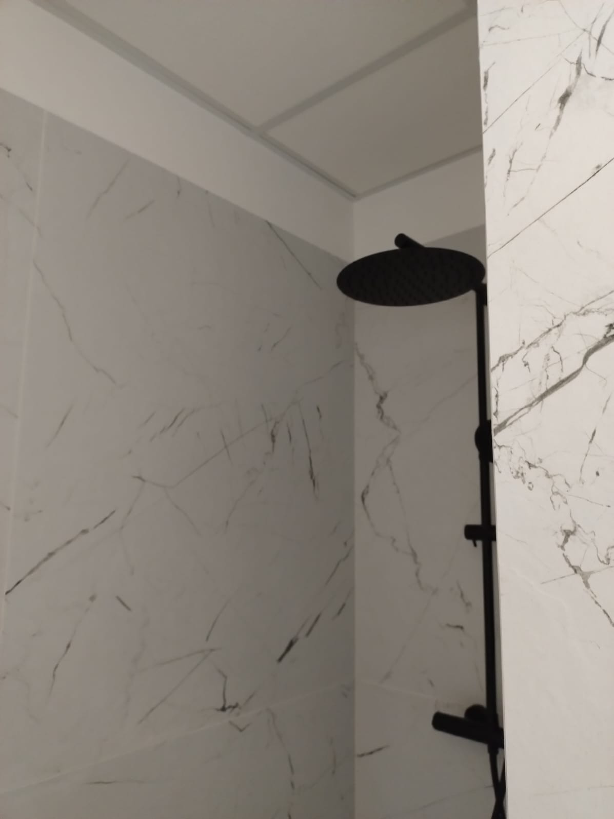 Wykończona łazienka: czarna deszczownica na tle białych płytek imitujących marmur. Minimalistyczny design i nowoczesne wykończenie.