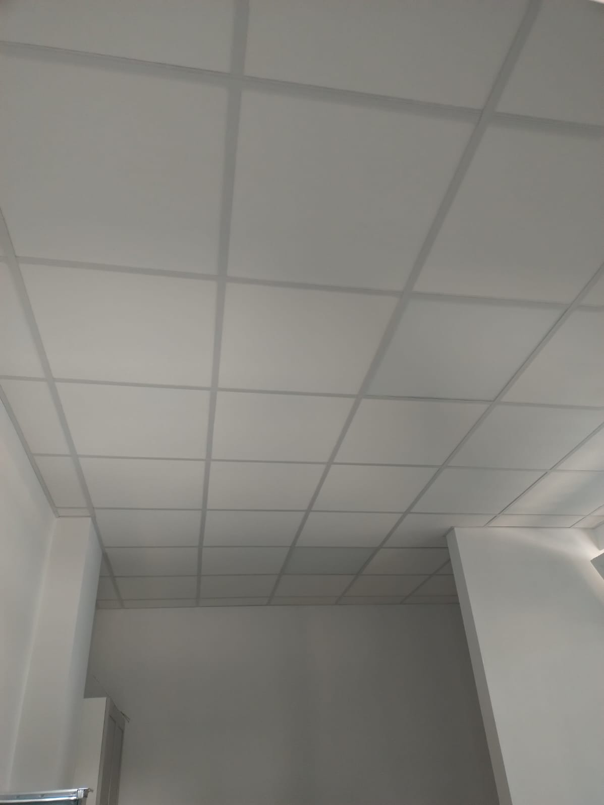 Biały sufit podwieszany kasetonowy z widoczną konstrukcją nośną, oświetlenie górne. Widok z dołu, proste linie, symetryczny układ.